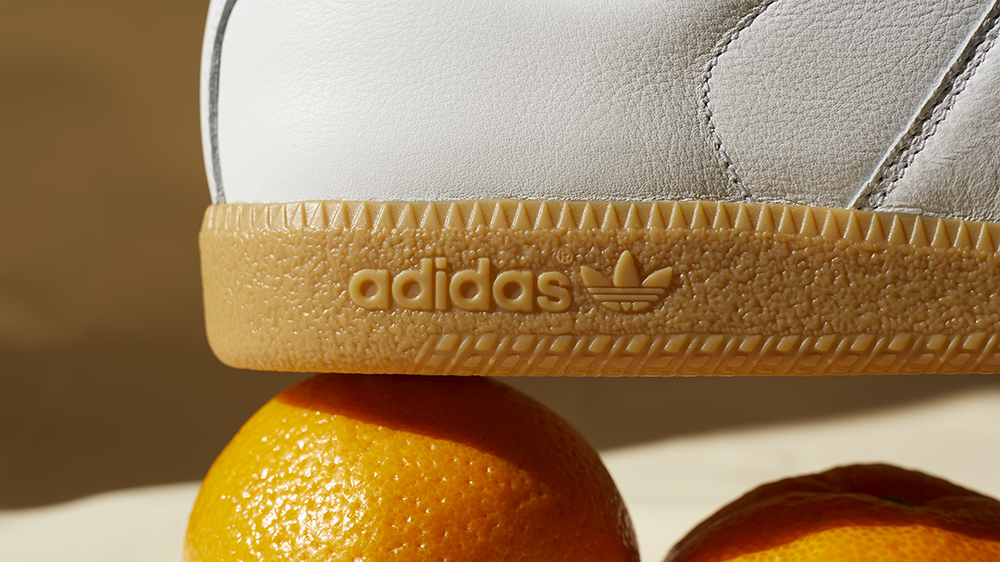 A still life image of adidas trainers sat on top of fruit with hard window light